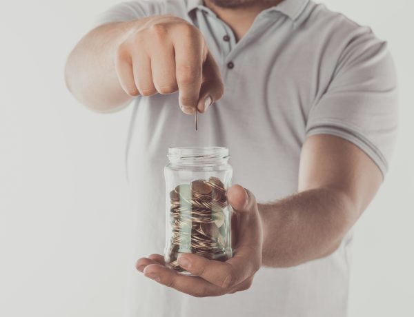 cropped image of man putting coin into jar isolated on white, saving concept