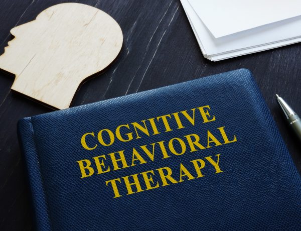 Cognitive Behavioral Therapyy CBT book and wooden head shape.