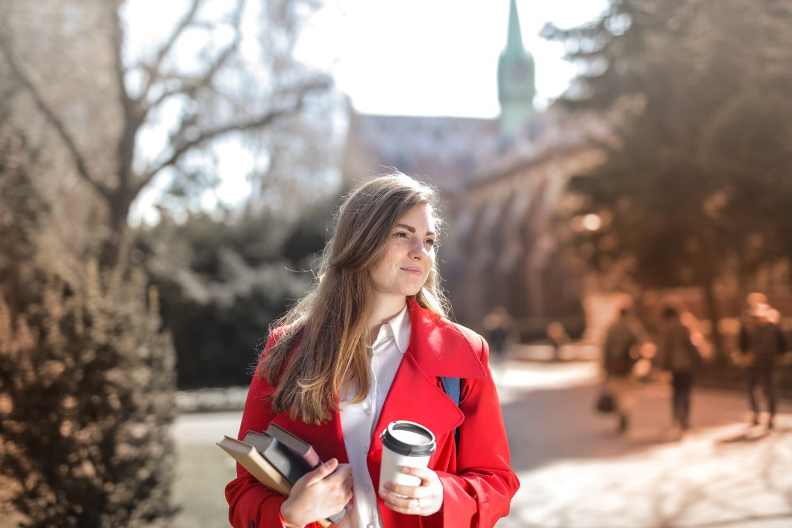 Woman in red coat holding notebooks and coffee cup