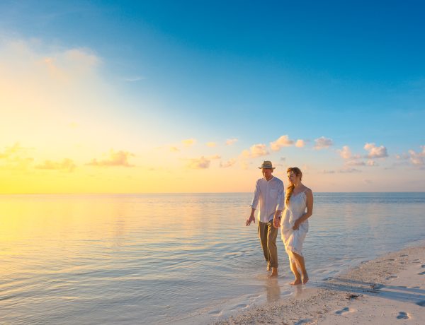 Couple walking on seashore wearing white tops during sunset