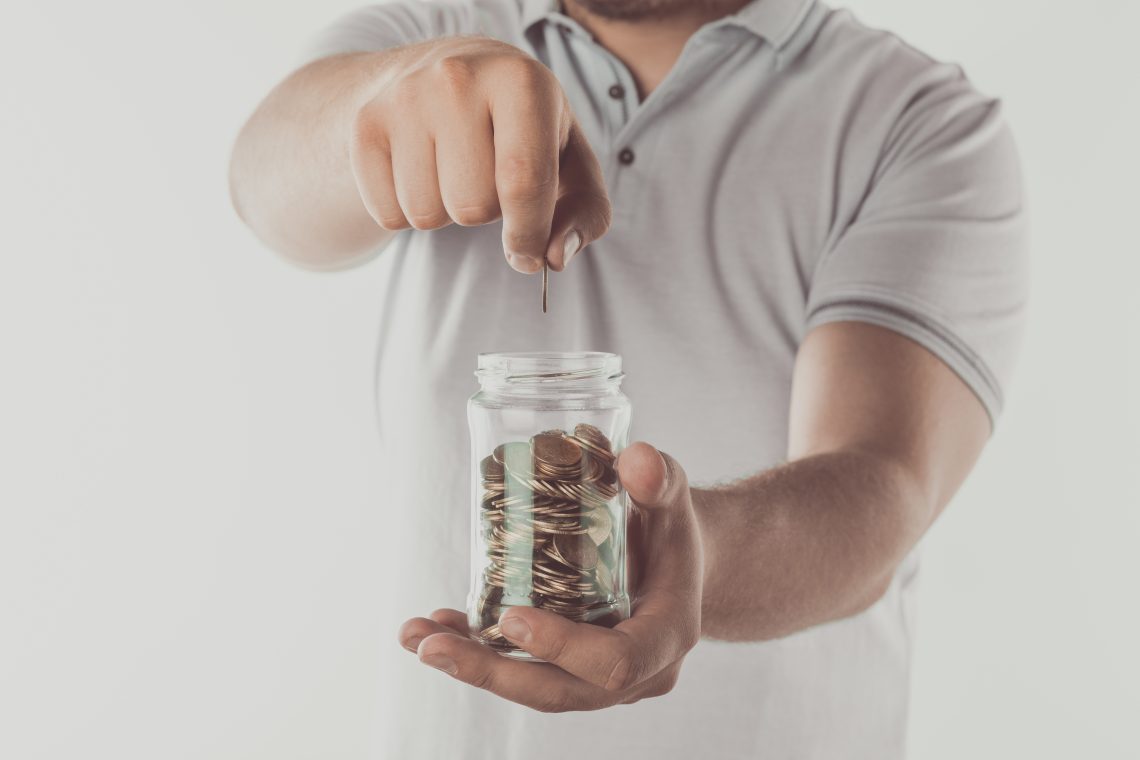 cropped image of man putting coin into jar isolated on white, saving concept