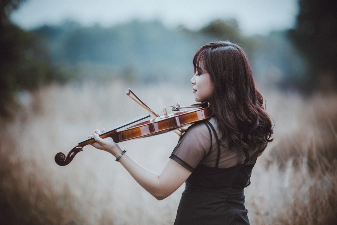 Stylish asian violinist playing violin in field in countryside