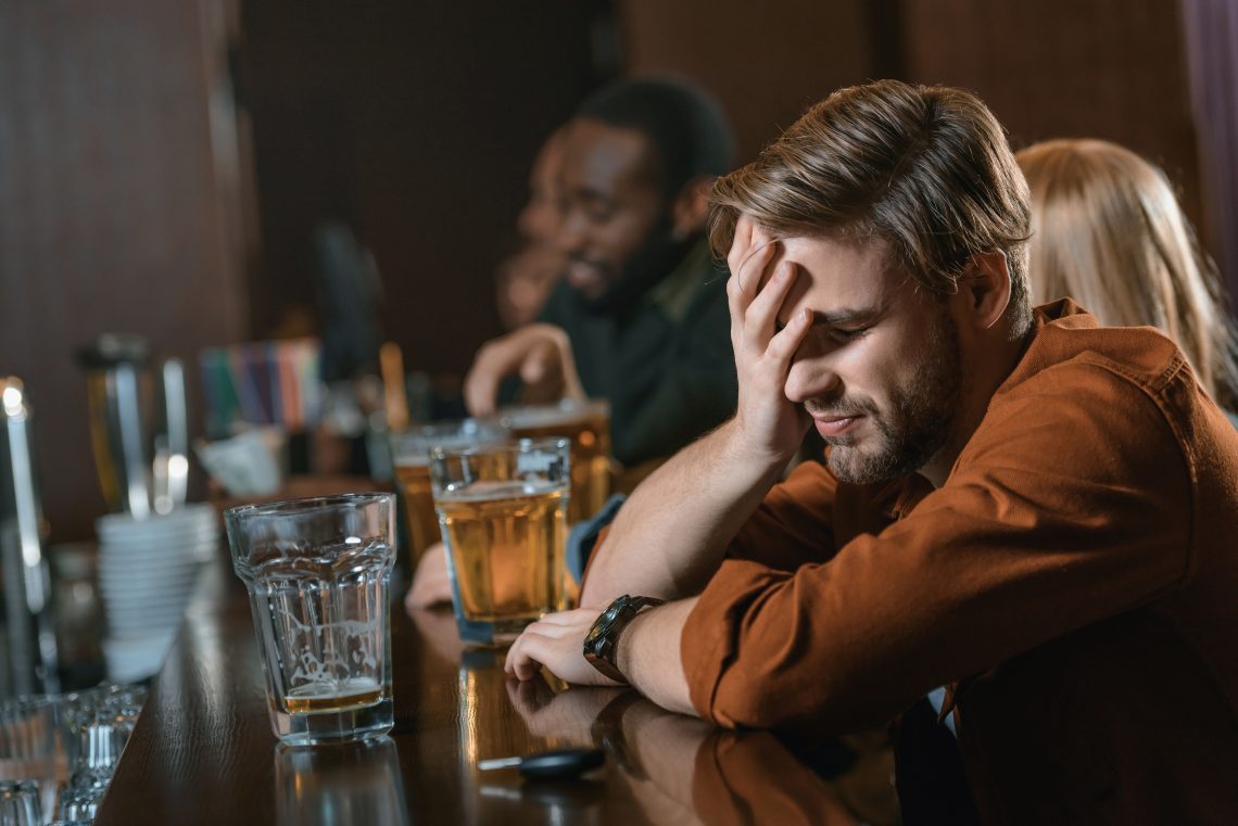 very drunk caucasian man with automobile keys at bar with friends