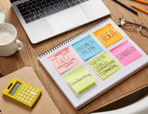 paper stickers with business strategy, calculator, cup of coffee and laptop on tabletop