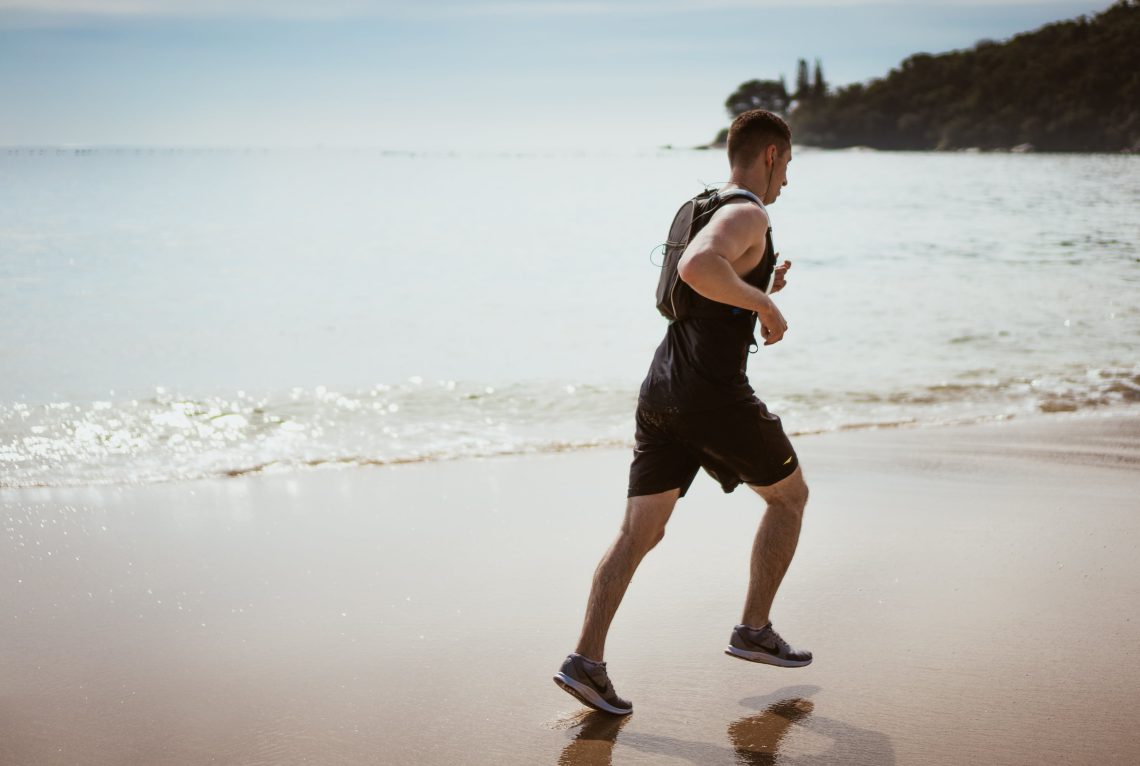 Man wearing black tank top and running on seashore