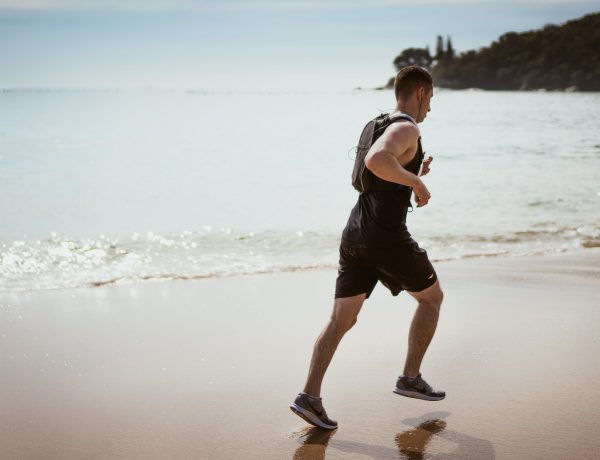 Man wearing black tank top and running on seashore