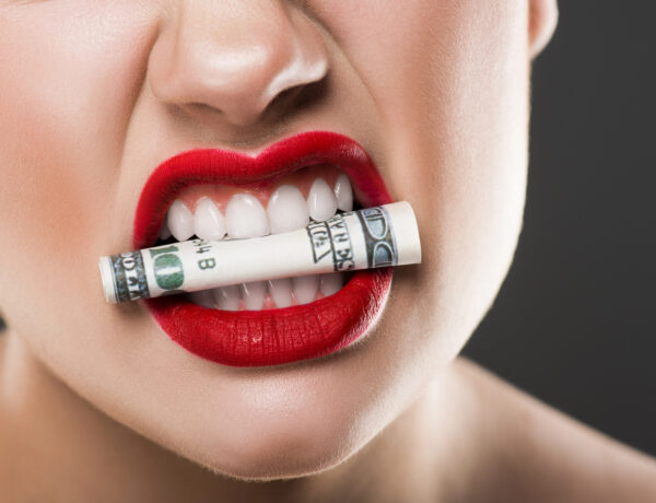 partial view of angry girl holding dollar banknote in teeth, isolated on grey