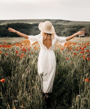 Elegant woman in hat walking in field with flowers
