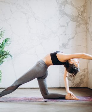 Woman in gray leggings and black sports bra doing yoga on yoga mat