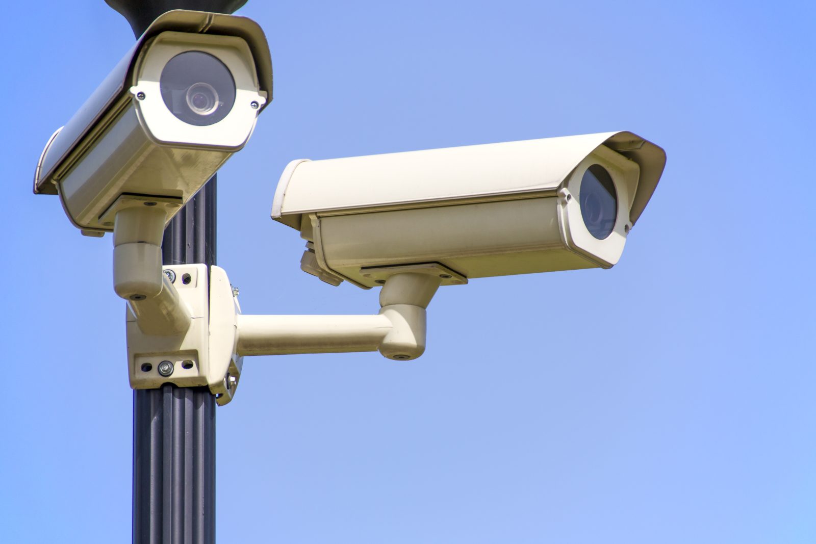 White 2 cctv camera mounted on black post under clear blue sky