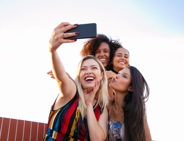 Cheerful multiethnic girlfriends taking selfie on smartphone on sunny day