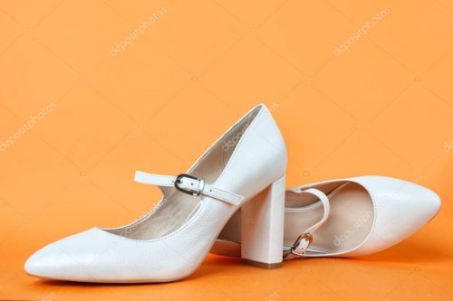 White high heel women's shoes on a orange background. Side view, close up.