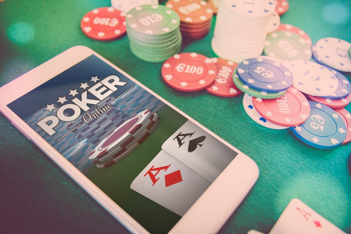 smartphone with poker website on screen, chips and cards over green poker table