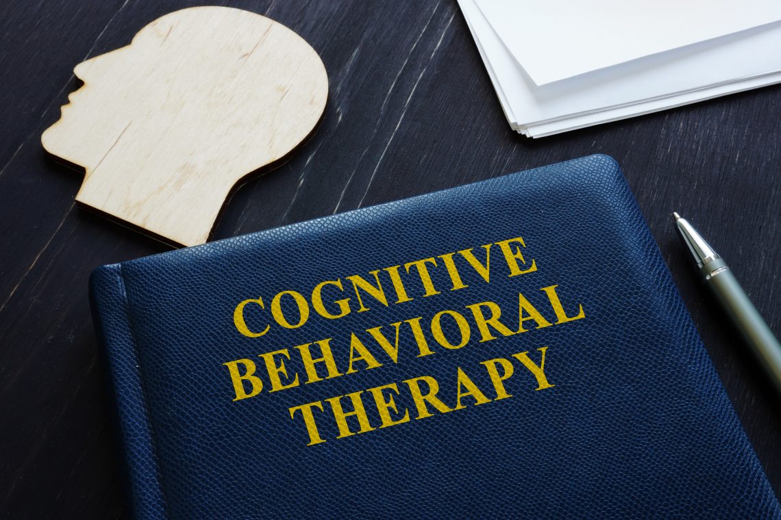 Cognitive Behavioral Therapyy CBT book and wooden head shape.