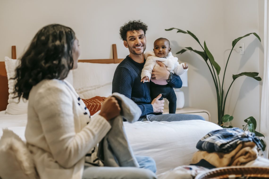 Happy ethnic father with infant in bedroom with black mother