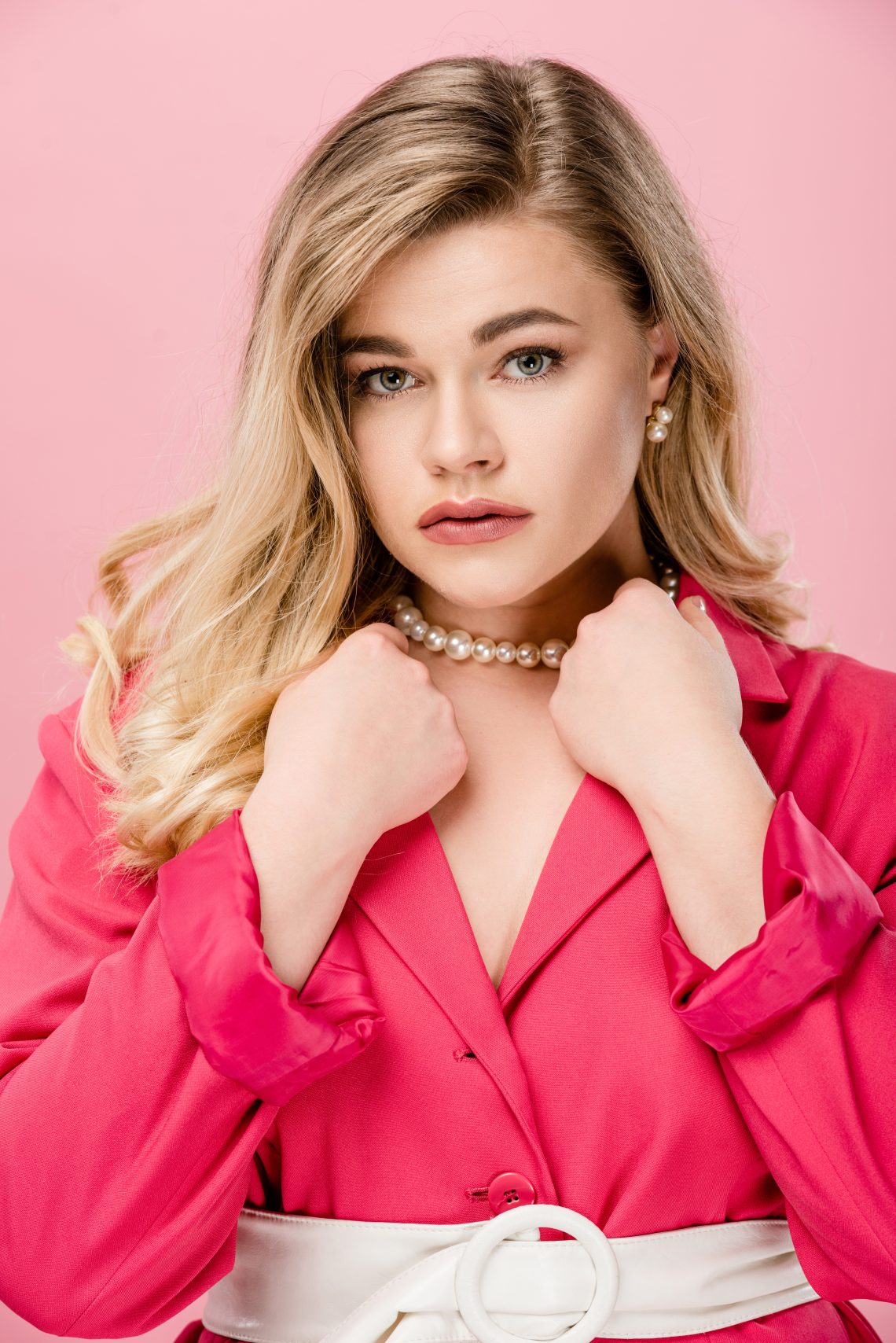 beautiful young woman in pink trench coat looking at camera isolated on pink