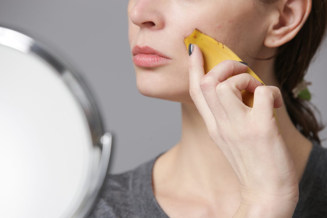 Woman rubbing banana peel on her face to brighten and hydrate skin and reduce wrinkles. Zero waste and natural skin care concept.