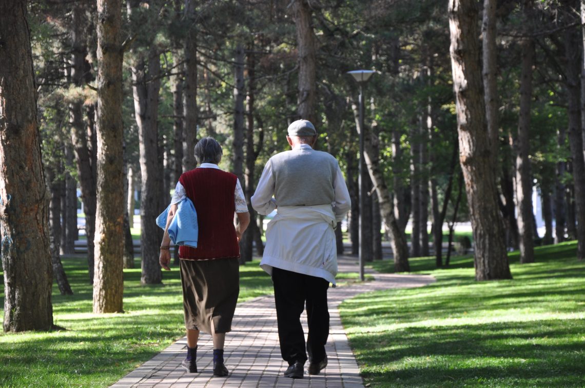 A man and a woman walking on pathway in between trees