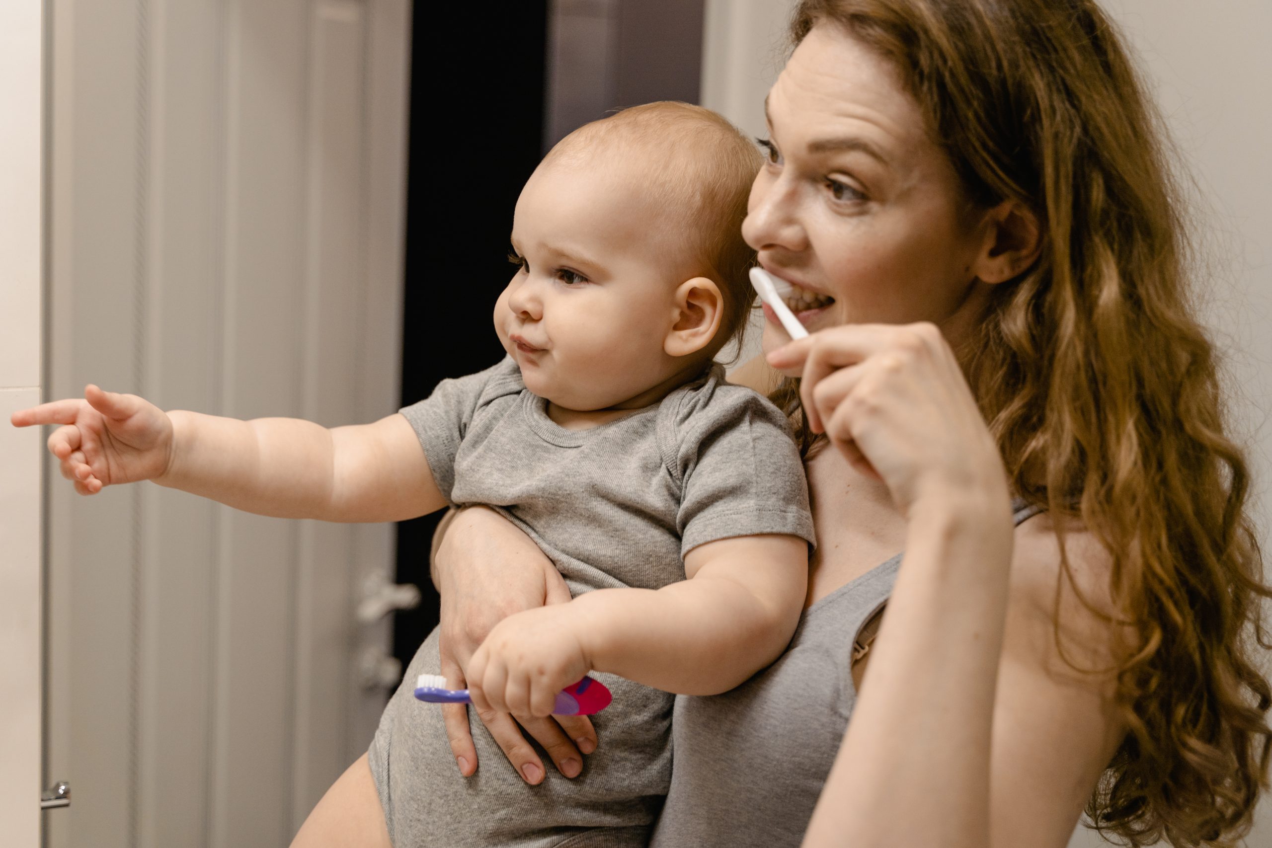 Close up photo of a mother carrying her baby while brushing her teeth