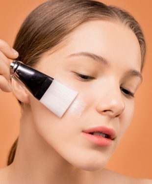 Woman applying moisturizer on her face using brush