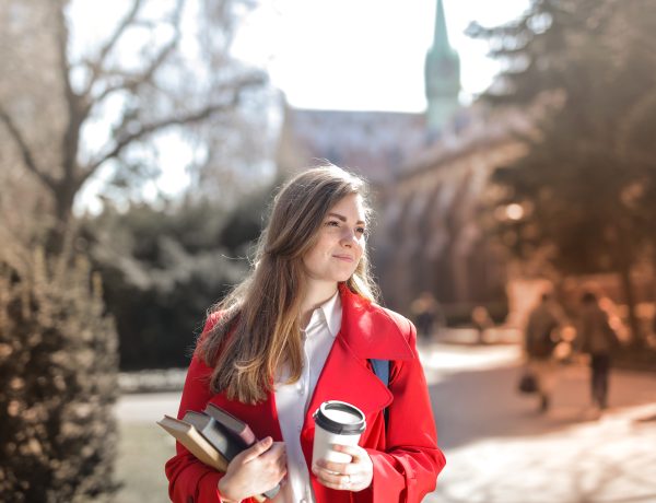 Woman in red coat holding notebooks and coffee cup