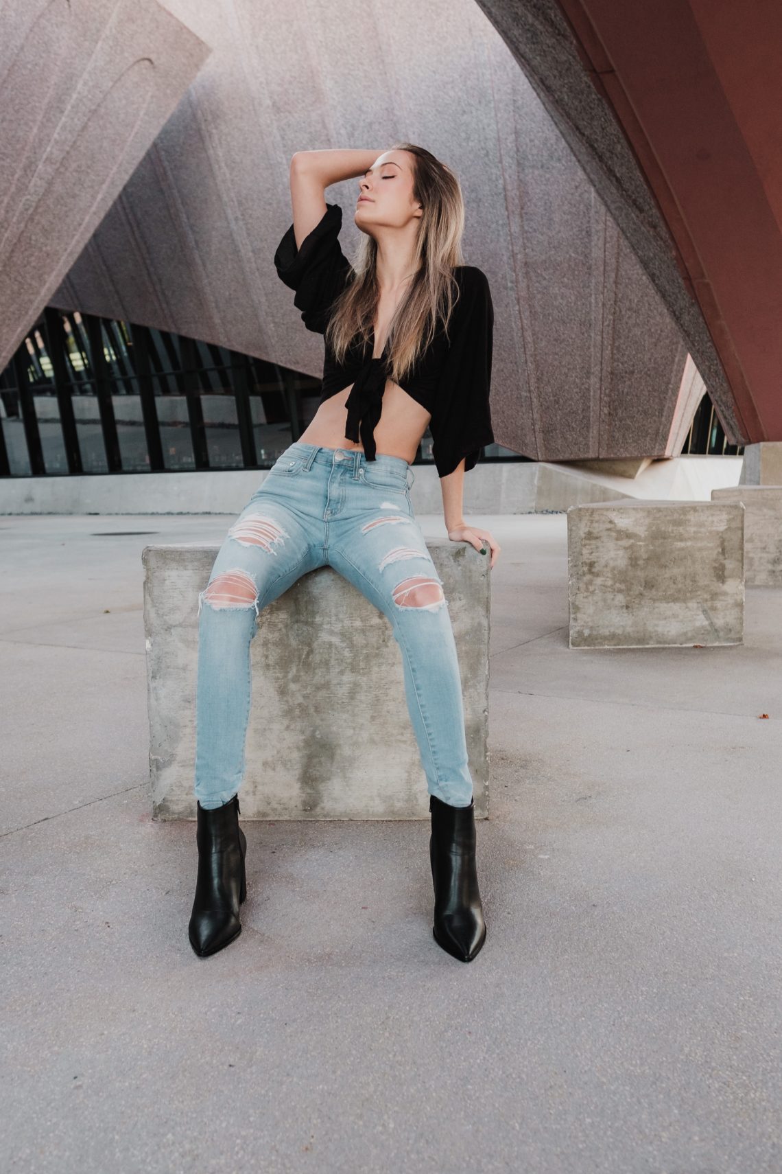 Woman in black crop top and blue denim jeans sitting on concrete bench