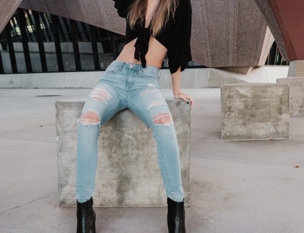 Woman in black crop top and blue denim jeans sitting on concrete bench