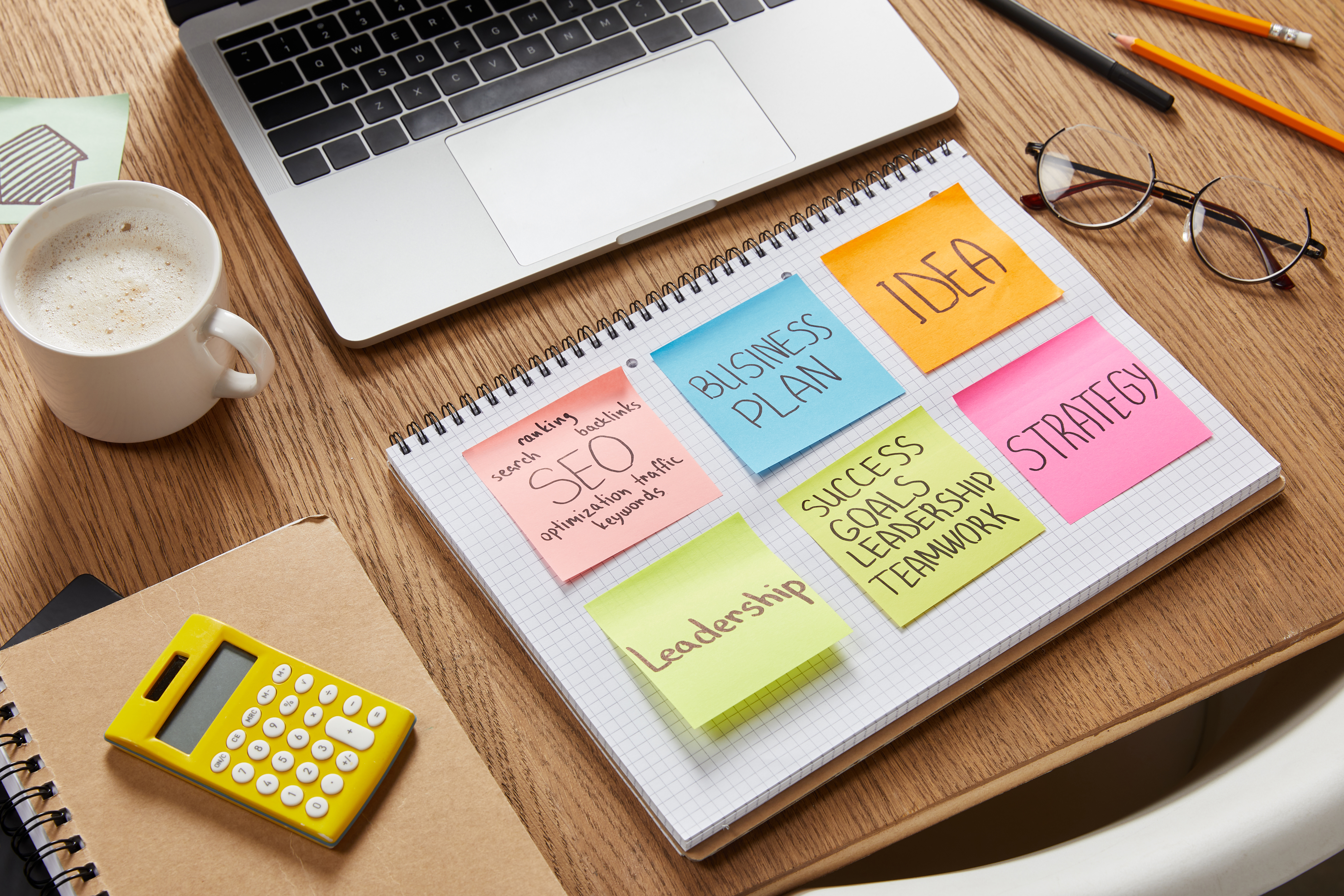 paper stickers with business strategy, calculator, cup of coffee and laptop on tabletop