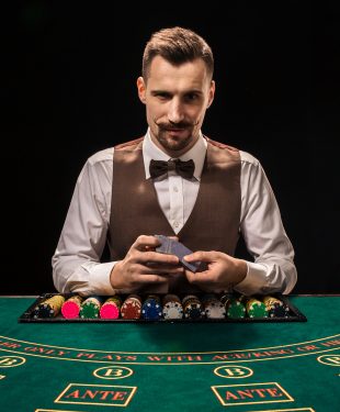 Handsome dealer shuffling playing cards deck and chips on green table