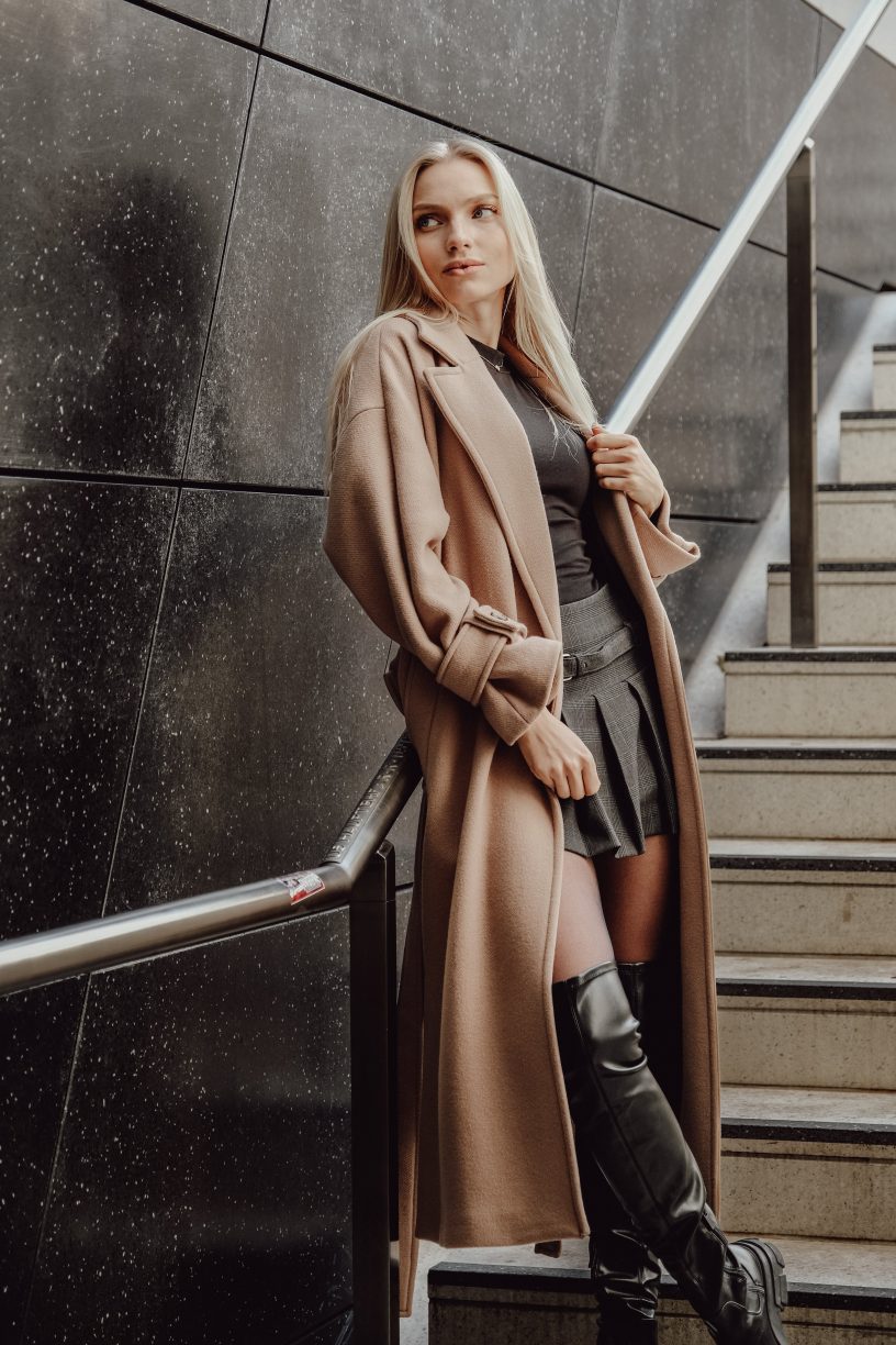 Person posing on steps in a trench coat looking sideways