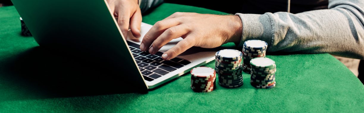 panoramic shot of man typing on laptop near poker chips